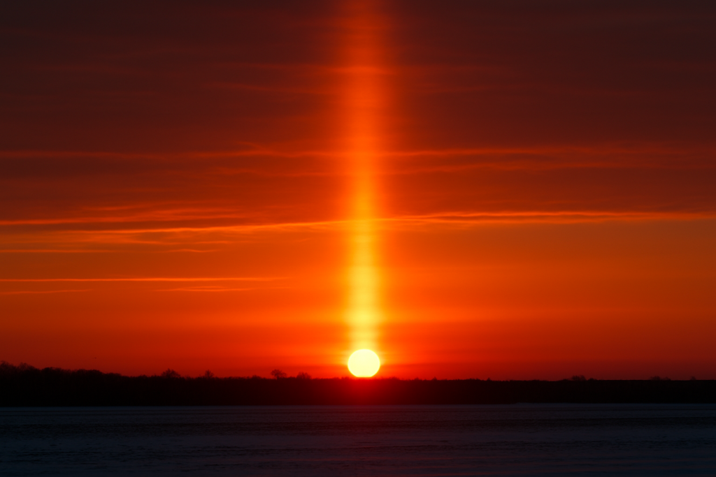 عمود ضوئي عمودي متوهج فوق الشمس عند الغروب في ظاهرة تُعرف بأعمدة الشمس.